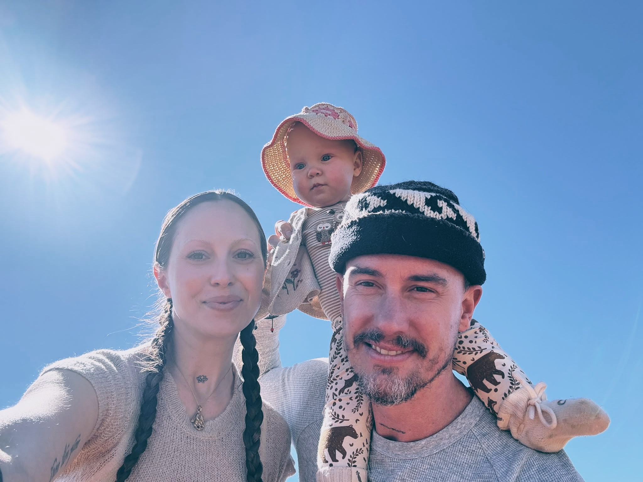 Maze and Mira with their child beneath a clear blue sky